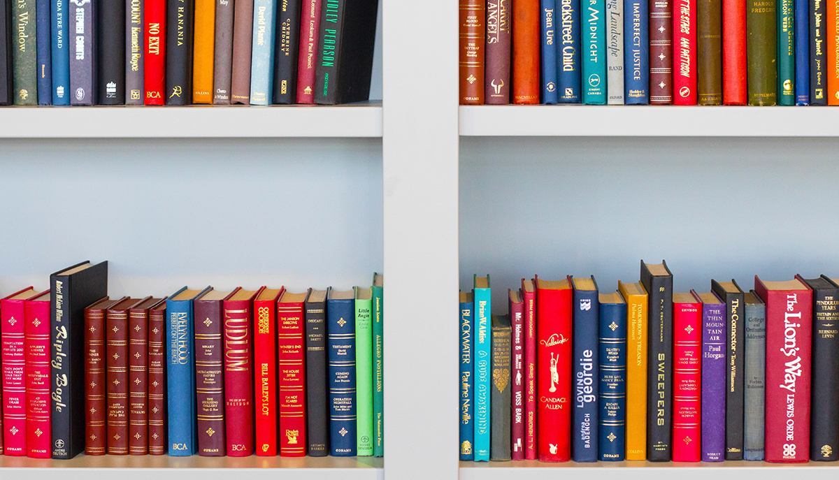 A photo of a bookshelf with various different sizes and colours of books.